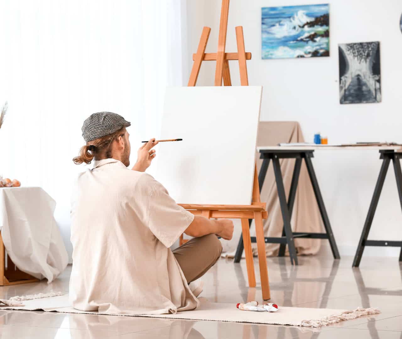 Man sat of the floor painting on a canvas